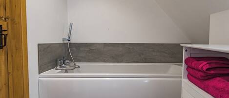 A modern bathroom with a white bathtub, a showerhead, and a wooden door.
