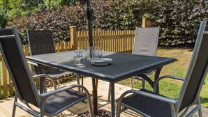 An outdoor patio with a table and chairs, surrounded by a wooden fence and lush greenery. - Charming barn conversion with enclosed private garden. (Sedlescombe)