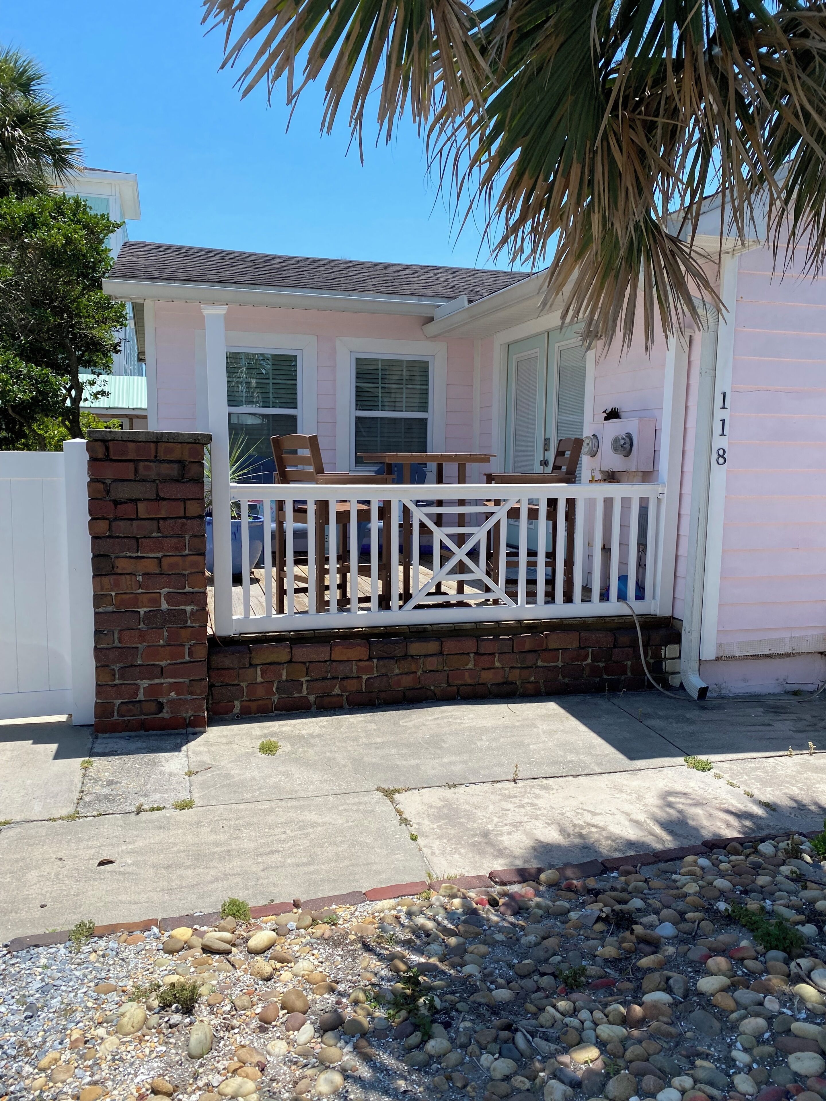 A residential house with a porch, a brick wall, and a white fence.