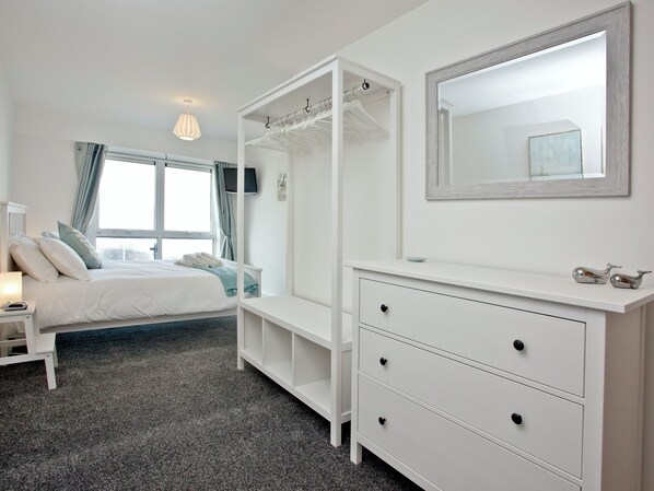 A bedroom with a bed, bedside table, dresser, mirror, and a window with curtains.
