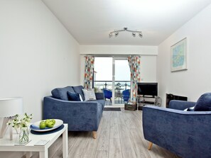 A modern living room with a sofa, armchairs, a TV, and a balcony with curtains.