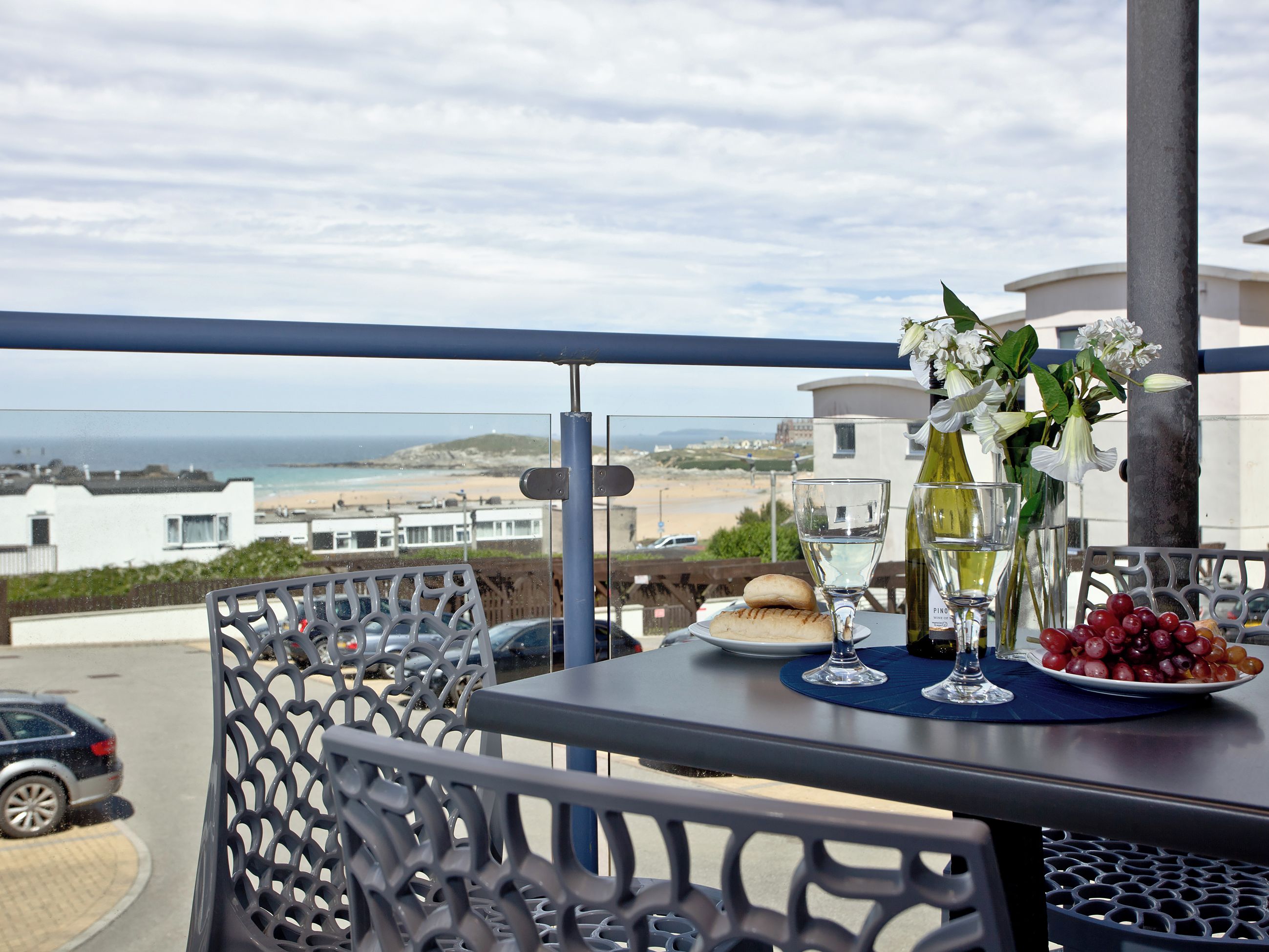 A balcony with a table set for two, overlooking a beach and buildings.