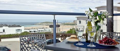 A balcony with a table set for two, overlooking a beach and buildings.