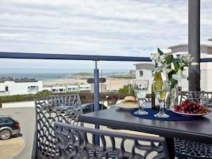 A balcony with a table set for two, overlooking a beach and buildings. - 2 bedroom accommodation in Newquay (Newquay)