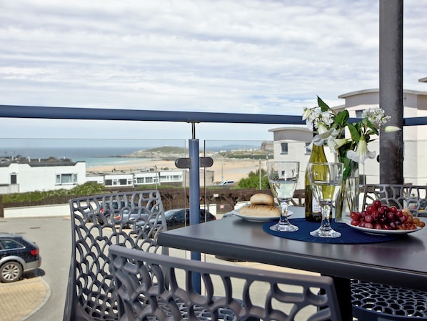 Un balcón con una mesa para dos, con vista a una playa y edificios.
