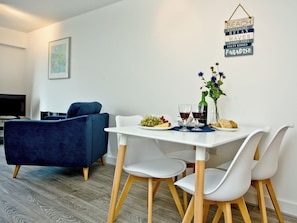 Un comedor con una mesa blanca, dos sillas blancas, un sofá azul y un cartel en la pared con palabras como 'BEACH' y 'PARADISE'.