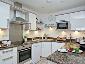 A modern kitchen with white cabinets, a stainless steel range hood, a built-in microwave, and a granite countertop.