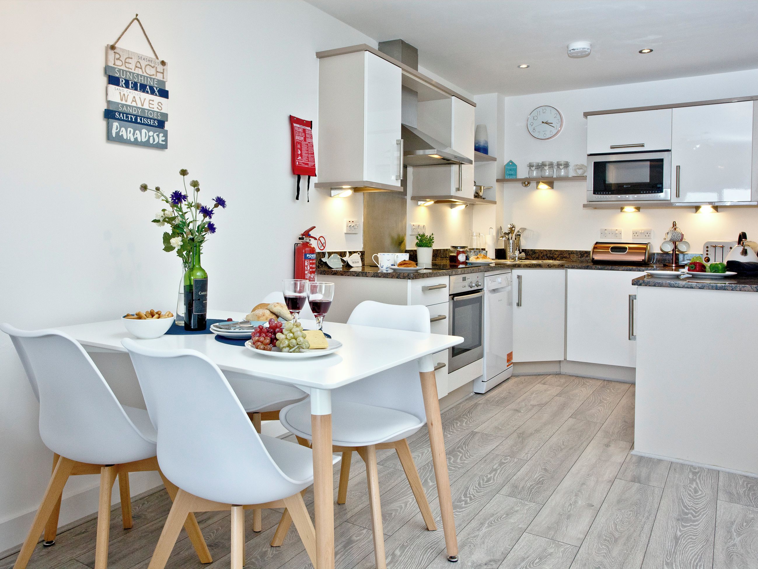 A modern kitchen with white cabinetry, a dining table with chairs, and a clock on the wall.