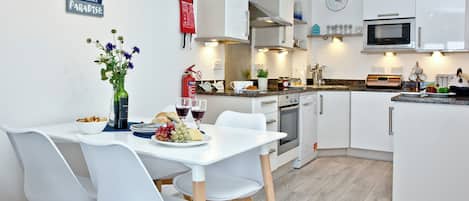 A modern kitchen with white cabinetry, a dining table with chairs, and a clock on the wall.