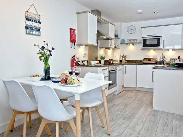 A modern kitchen with white cabinetry, a dining table with chairs, and a clock on the wall.