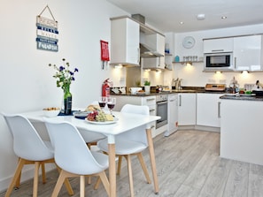 A modern kitchen with white cabinetry, a dining table with chairs, and a clock on the wall. - 2 bedroom accommodation in Newquay (Newquay)