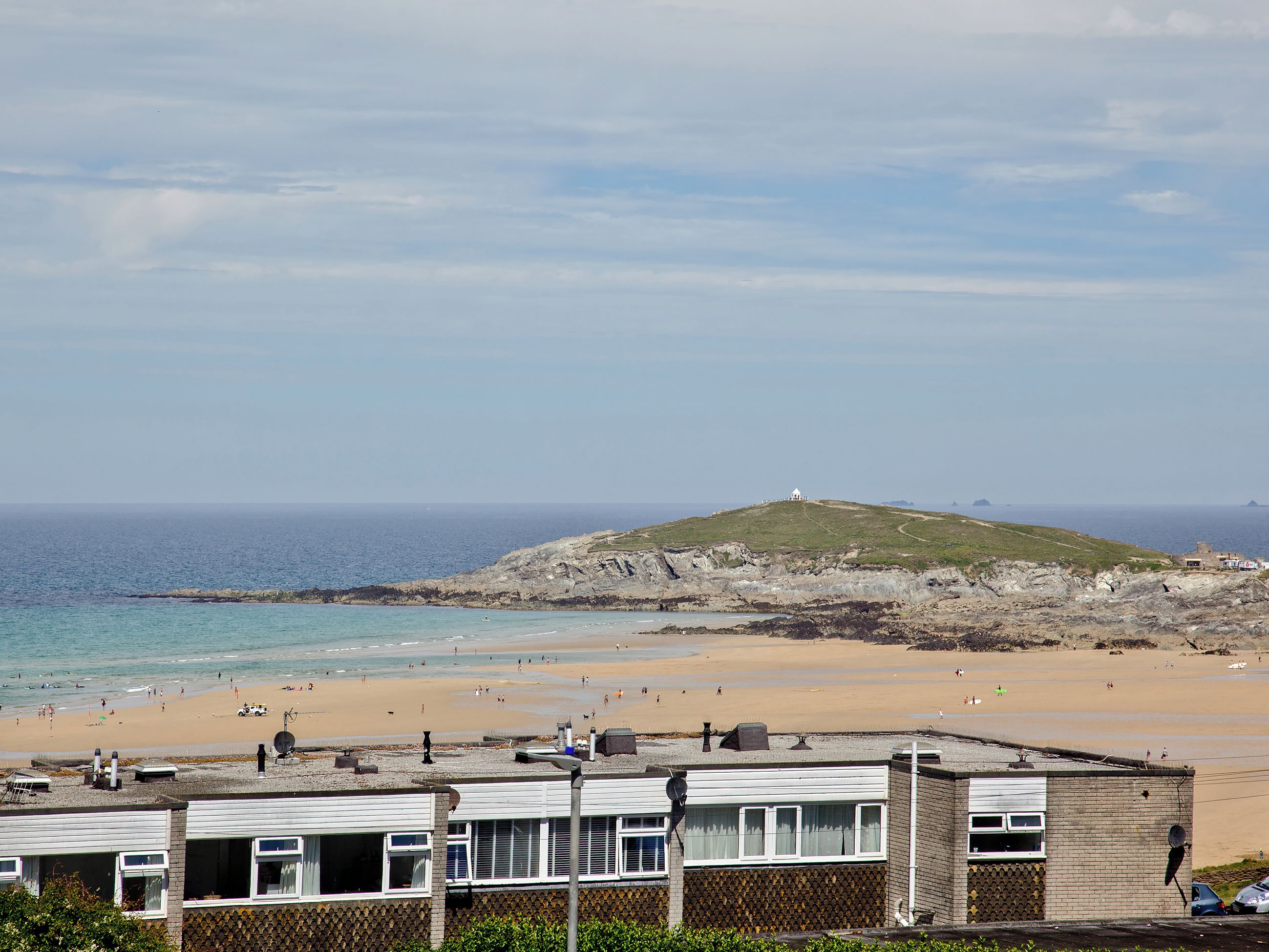 A coastal view with a beach, a hill with a structure, and buildings in the foreground.