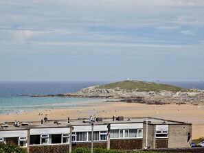 Vista costera con playa, una colina con una edificación y edificios en primer plano.