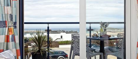Un balcon avec vue sur la mer, une plante en pot et du mobilier d’extérieur.