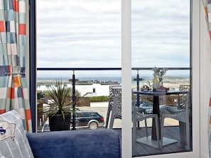 Un balcón con vista al mar, una planta en maceta y mobiliario exterior.