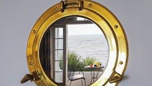 A round, brass-framed mirror with a view of the sea through an open door. - 1 bedroom accommodation in Sandgate (Sandgate)