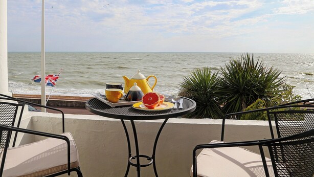 A balcony with a table set for breakfast overlooking the sea, featuring a flag, a teapot, and a fruit. - 1 bedroom accommodation in Sandgate (Sandgate)