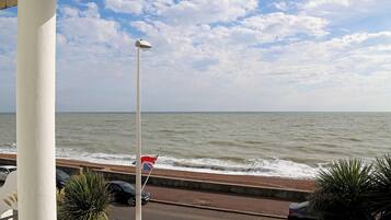 A view of the sea from a balcony with a street and parked cars in the foreground.
