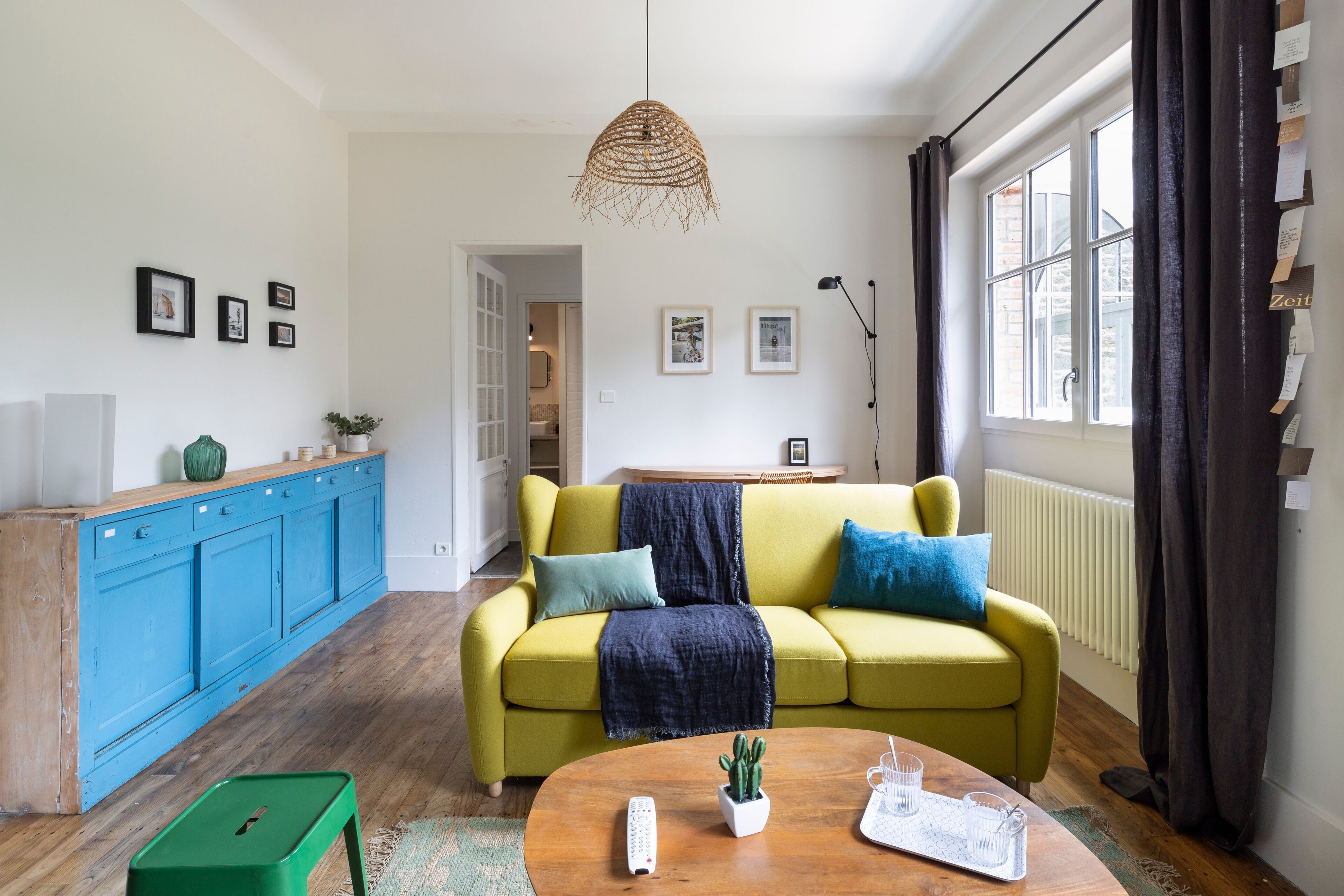 Ein helles Wohnzimmer mit einem gelben Sofa, einem Holztisch und einem blauen Schrank.