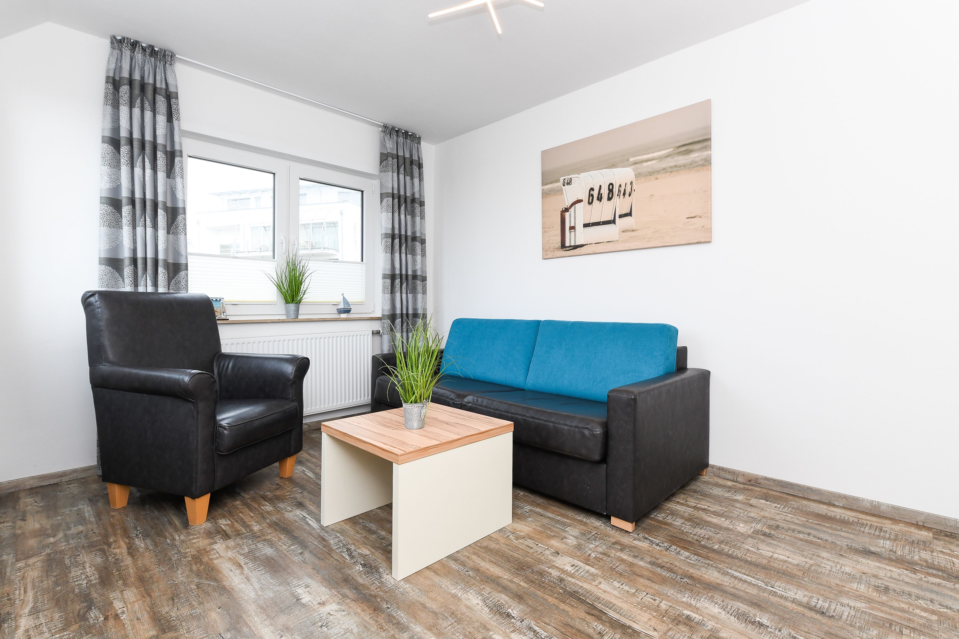 Een woonkamer met een zwarte leren fauteuil, een blauwe bank en een houten salontafel.