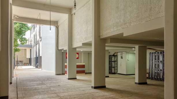 A spacious indoor corridor with tiled flooring, large pillars, and a visible reception area in the distance.