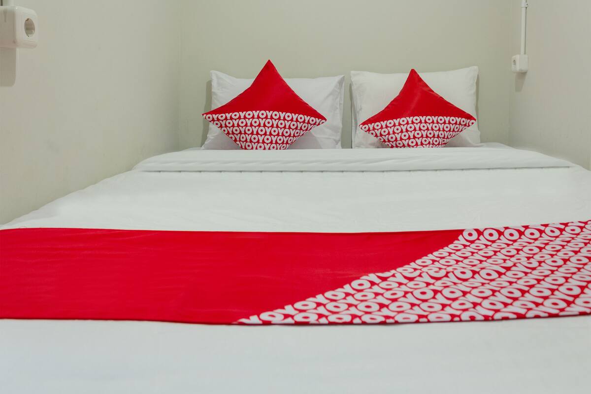 A bed with white bedding and red pillows with a pattern.