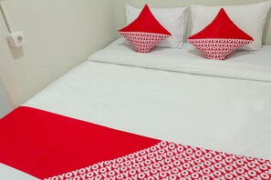 A bed with white bedding and two red pillows with a repeated pattern. - OYO 737 Kamar Keluarga Mahkota 8 (Tangerang)