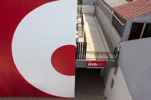 A building with a large red and white circular sign, a balcony with a metal railing, and a red sign with white text on the wall. - OYO 737 Kamar Keluarga Mahkota 8 (Tangerang)