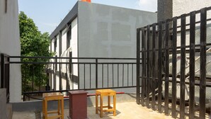 A balcony with two wooden stools and a red table, enclosed by a black metal fence.