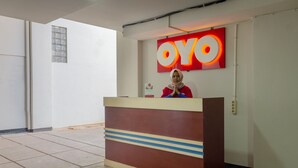 A reception desk with a 'OYO' sign, a person in a red uniform, and a tiled floor.