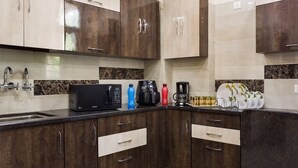 A modern kitchen with dark wood cabinets, a black microwave, a coffee maker, and a sink. - ACHLA PARADISE – LUXURY 2BHK APARTMENT (4 BEDS) (New Delhi)