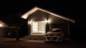Une maison de nuit avec une voiture blanche garée dans l’allée.