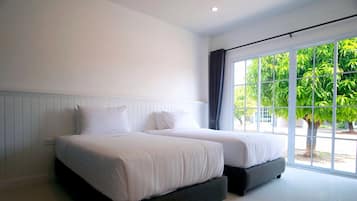 A hotel room with two beds, a large window with a view of greenery, and a white wall.