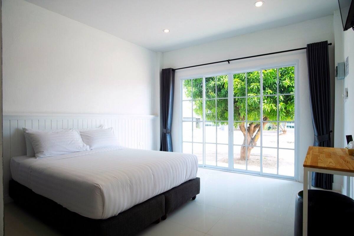 A bedroom with a bed, a window with curtains, and a view of greenery outside.