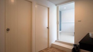 Un couloir avec deux portes fermées, une petite fenêtre et une poubelle.