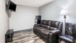 Una sala de estar moderna con un sofá de cuero, una mesita negra, un televisor montado en la pared, un microondas, un refrigerador y una lámpara de pie.