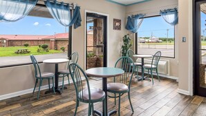 Un interior de restaurante con sillas color turquesa, mesas redondas y ventanas amplias con cortinas azules.