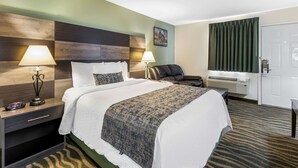 Una habitación de hotel con cama, lámparas de noche, una silla, un escritorio y una puerta.