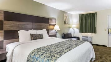 Ein Hotelzimmer mit einem großen Bett, einem Schreibtisch, einem Sessel, einer Lampe und einer Klimaanlage.