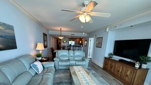 A living room with a sofa, a recliner, a coffee table, a TV, and a ceiling fan.
