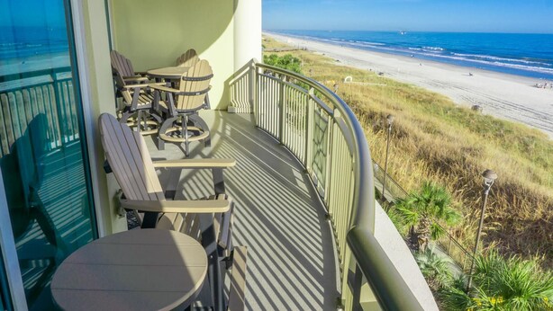 A balcony with outdoor furniture overlooking a beach.