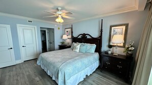 A bedroom with a bed, a ceiling fan, a nightstand, a dresser, and a door.