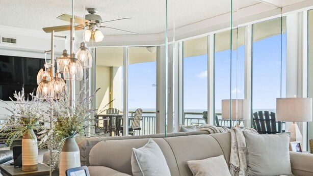 Ein modernes Wohnzimmer mit einer Couch, einem Deckenventilator und einem großen Fenster mit Meerblick.