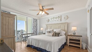 Ein Schlafzimmer mit Bett, Nachttischen, Deckenventilator, Fenster mit Blick und einem Holzschrank.