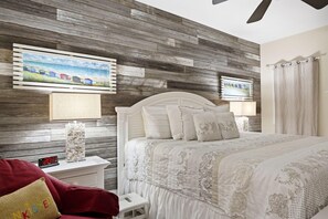 Une chambre avec un mur en bois, un lit avec une literie blanche, une table de chevet avec une horloge et une chaise rouge.
