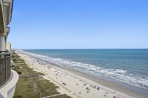 Uma praia com uma extensa faixa de areia, alguns guarda-sóis e um edifício à esquerda.