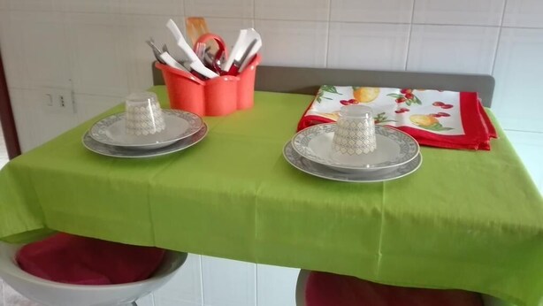 A kitchen with a green tablecloth, two grater plates, a red napkin holder, and a fruit-patterned tablecloth. - Vacation home !! (Trappeto)