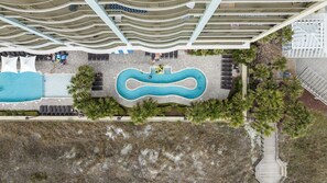 An aerial view of a resort with a central swimming pool, lounge areas, and a distinctive wave-like roof structure. - MVG 1116 4 Bedroom Ocean View (North Myrtle Beach)