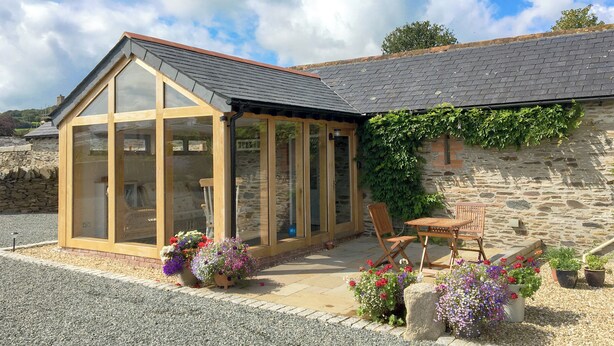 A glass-roofed structure adjacent to a stone building with a gravel driveway and potted plants. - 2 bedroom accommodation in North Hill (North Hill)