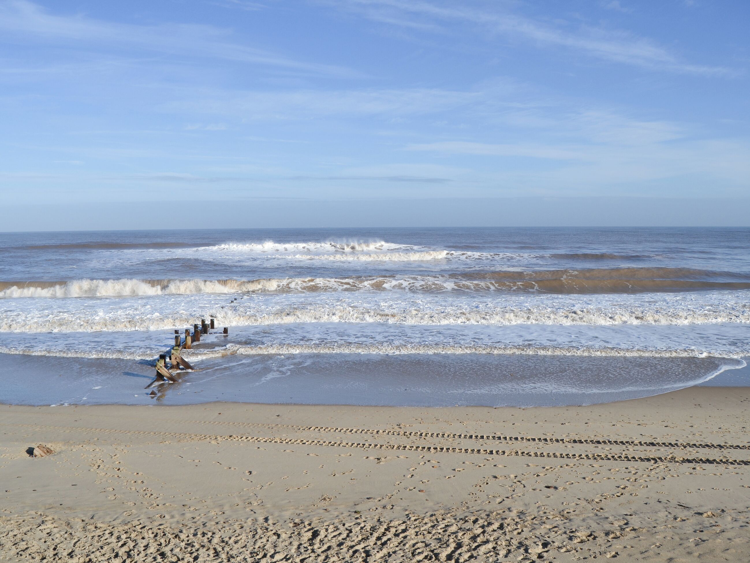 Ein Strand mit Fußabdrücken, die zum Wasser führen, Wellen, die an die Küste schlagen, und einem klaren Himmel.